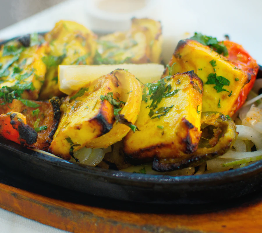 Smoky paneer tikka with charred peppers and onions on a sizzling plate